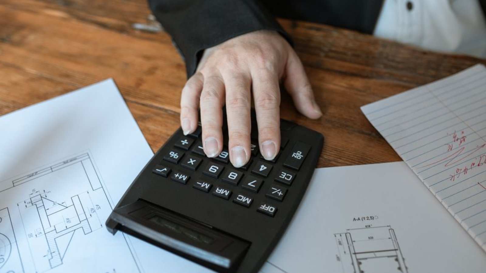 Des notes manuscrites, une calculatrice et un stylo posés sur un bureau en bois.