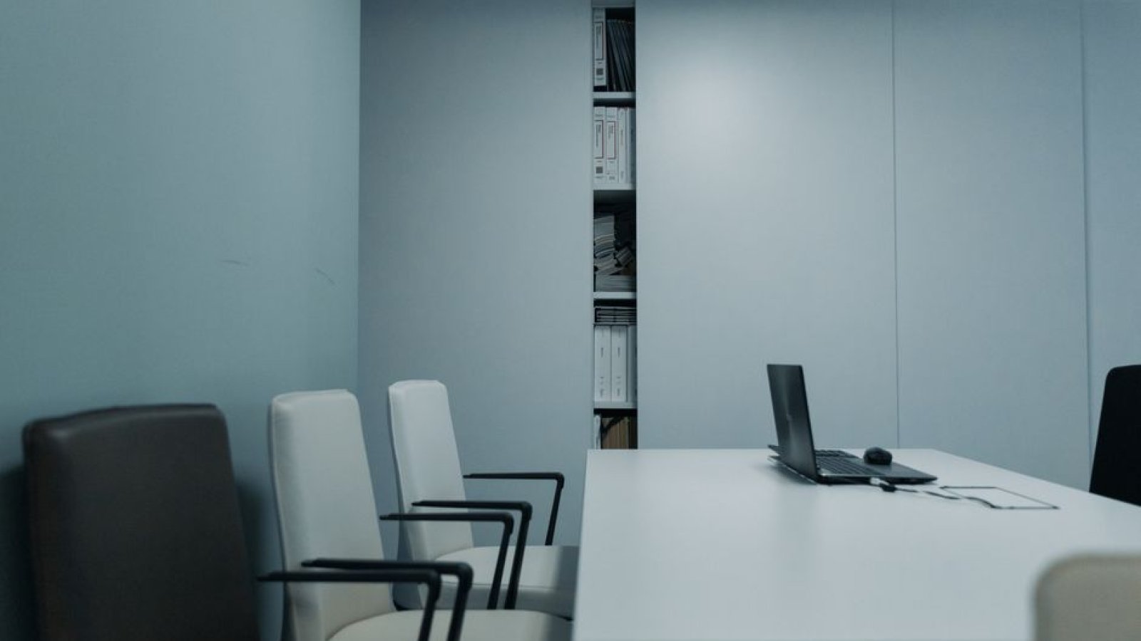 Une salle de réunion vide, table et chaises alignées, dans la lumière du jour.